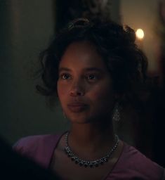 a woman in a pink shirt and necklace looking at the camera with an intense look on her face