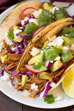 two tacos on a white plate with lime wedges