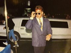 a man in a suit and tie standing next to a white car while talking on a cell phone