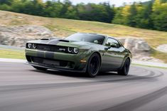 a green sports car driving on a road with trees in the backgrouund