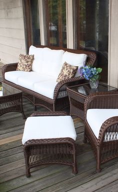 a wicker couch and chair sitting on a wooden deck with white cushions, in front of a window