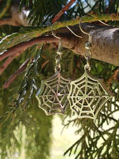 two silver spider web earrings hanging from a tree branch in front of some branches with green leaves