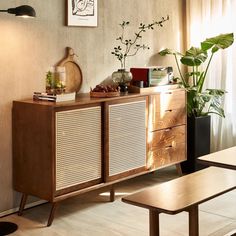 a living room with a wooden cabinet and plants on the sideboard next to a window