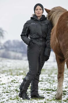 a woman standing next to a brown horse on top of a snow covered grass field