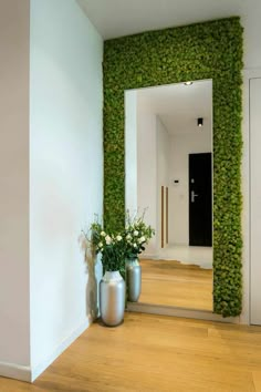 two vases filled with flowers sitting on top of a wooden floor next to a wall