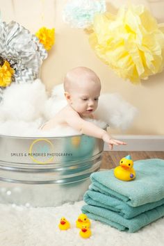 a baby in a bath tub surrounded by yellow rubber ducky toys and blue towels