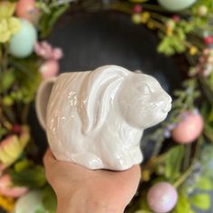 a hand holding a white ceramic dog figurine in front of a wreath