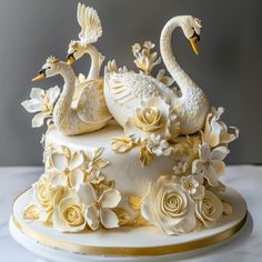 two white swans sitting on top of a cake covered in frosting flowers and leaves