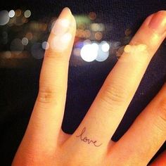 a person's hand with a small tattoo on the middle finger that says love