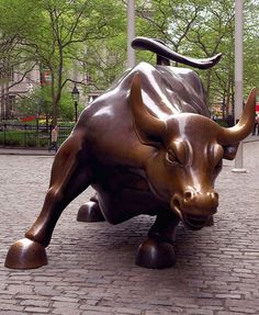 a statue of a bull is on the ground in front of a brick walkway and trees