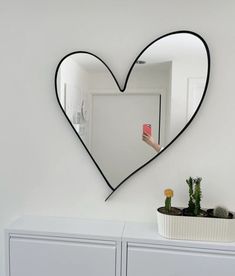 a heart shaped mirror hanging on the side of a wall next to a white cabinet