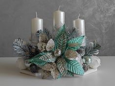 some candles are sitting on a table with silver and green decorations around it, along with pine cones