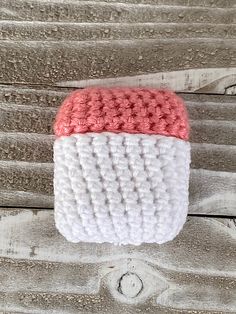 a white and pink knitted object sitting on top of a wooden table next to a piece of wood