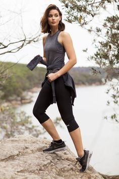 a woman standing on top of a rock next to a lake and holding an object in her hand