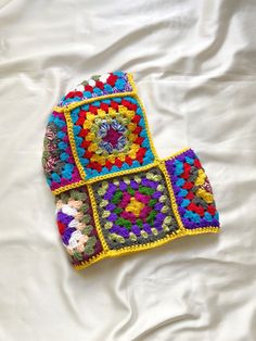 a multicolored crocheted bag laying on top of a white sheet covered bed