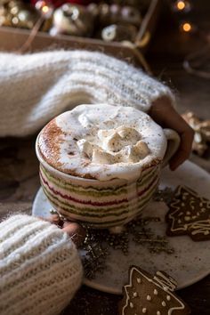 a cup of hot chocolate with whipped cream on top and christmas decorations in the background