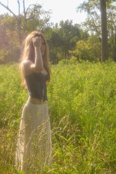 a woman standing in tall grass with her hands to her face and looking into the distance