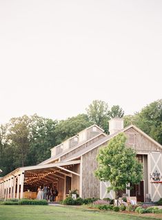 a barn with people standing on the front and side of it, surrounded by trees