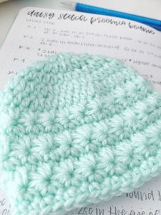 a crocheted hat sitting on top of a piece of paper next to a pen