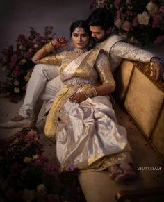 a man and woman sitting next to each other on a couch in front of flowers