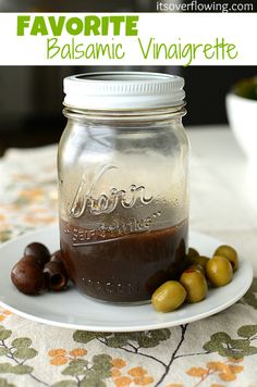 a jar filled with liquid sitting on top of a white plate next to some olives