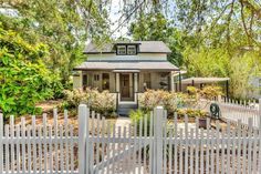 a white picket fence in front of a small house with trees and bushes around it