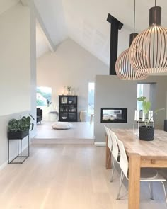 an open living room and dining area with white walls, wood flooring and modern lighting fixtures