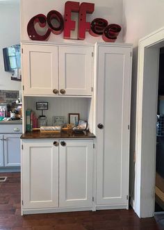 a kitchen with white cupboards and wooden flooring next to a coffee sign on the wall