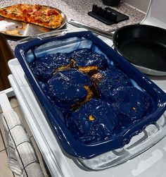 a blue pan sitting on top of a stove next to a pizza