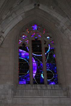 a large stained glass window in the side of a stone building with multiple colored lights on it