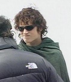 a man wearing sunglasses standing next to another man with long curly hair on his head