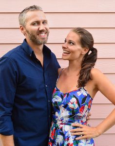 a man and woman standing next to each other in front of a pink wall smiling