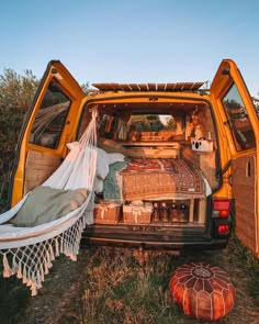 the back end of an orange van filled with luggage and blankets, sitting in a field