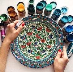 a woman is painting on a plate with paintbrushes and other items around it