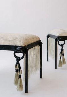 two stools with tassels on the legs and one has a black frame