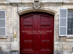 two red doors with the words departures print shop original print on them in front of an old building