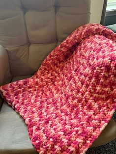 a pink and white crocheted blanket sitting on top of a couch next to a window