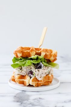 a waffle sandwich with chicken, lettuce and blueberries on a white plate