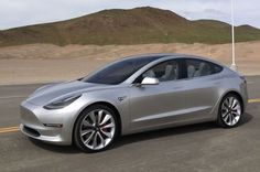 a silver tesla model 3 is parked on the side of the road with mountains in the background