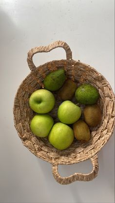 a wicker basket filled with green apples and kiwis on top of a white wall