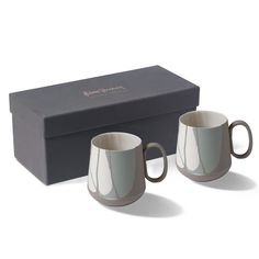 two coffee mugs sitting in front of a box with the lid open and one is empty