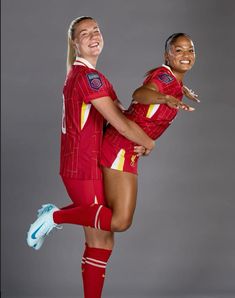 two female soccer players in red uniforms posing for the camera with their arms around each other