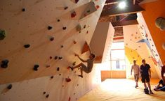 two men are climbing up the side of a rock wall in an indoor gym area