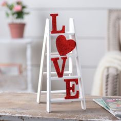 a white ladder with red glittered letters spelling love on the side and a pink flower pot next to it