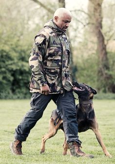 a man is walking with his dog on the grass in front of some trees and bushes