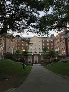 the walkway leading to an apartment building with trees on both sides and grass in front