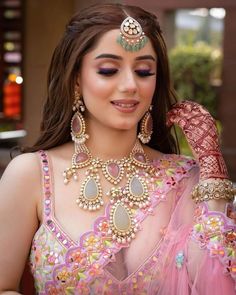 a woman in a pink outfit with jewelry on her neck and hands behind her head