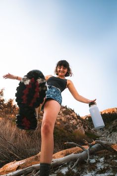 a woman in short shorts is holding a water bottle and standing on a rocky hill