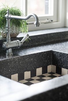 a kitchen sink with a black and white checkered counter top next to a window