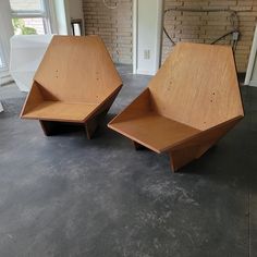 two wooden chairs sitting next to each other on top of a cement floor in front of a brick wall